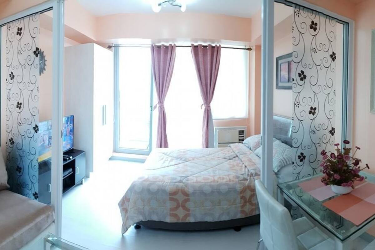 Un dormitorio con una cama, un sofá, una mesa de vidrio y un televisor.