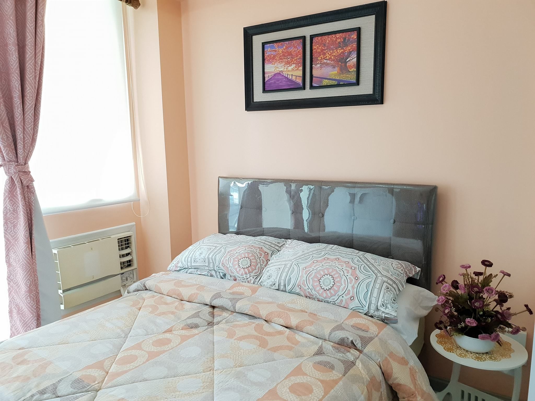 Una cama bien hecha con ropa de cama estampada, un cabecero con superficie reflectante y una obra de arte enmarcada encima.
