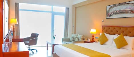 Una habitación de hotel con cama, mesita de noche, lámpara, silla y un amplio ventanal.
