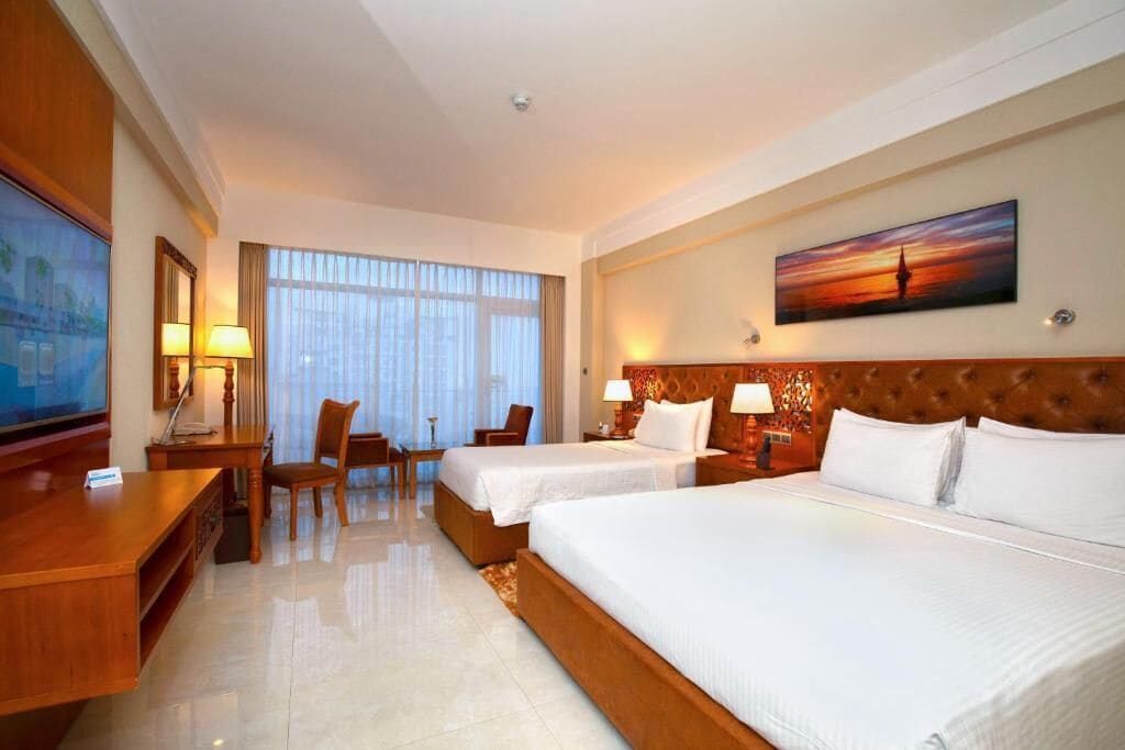 A hotel room with two beds, a desk, chairs, and a large painting on the wall.