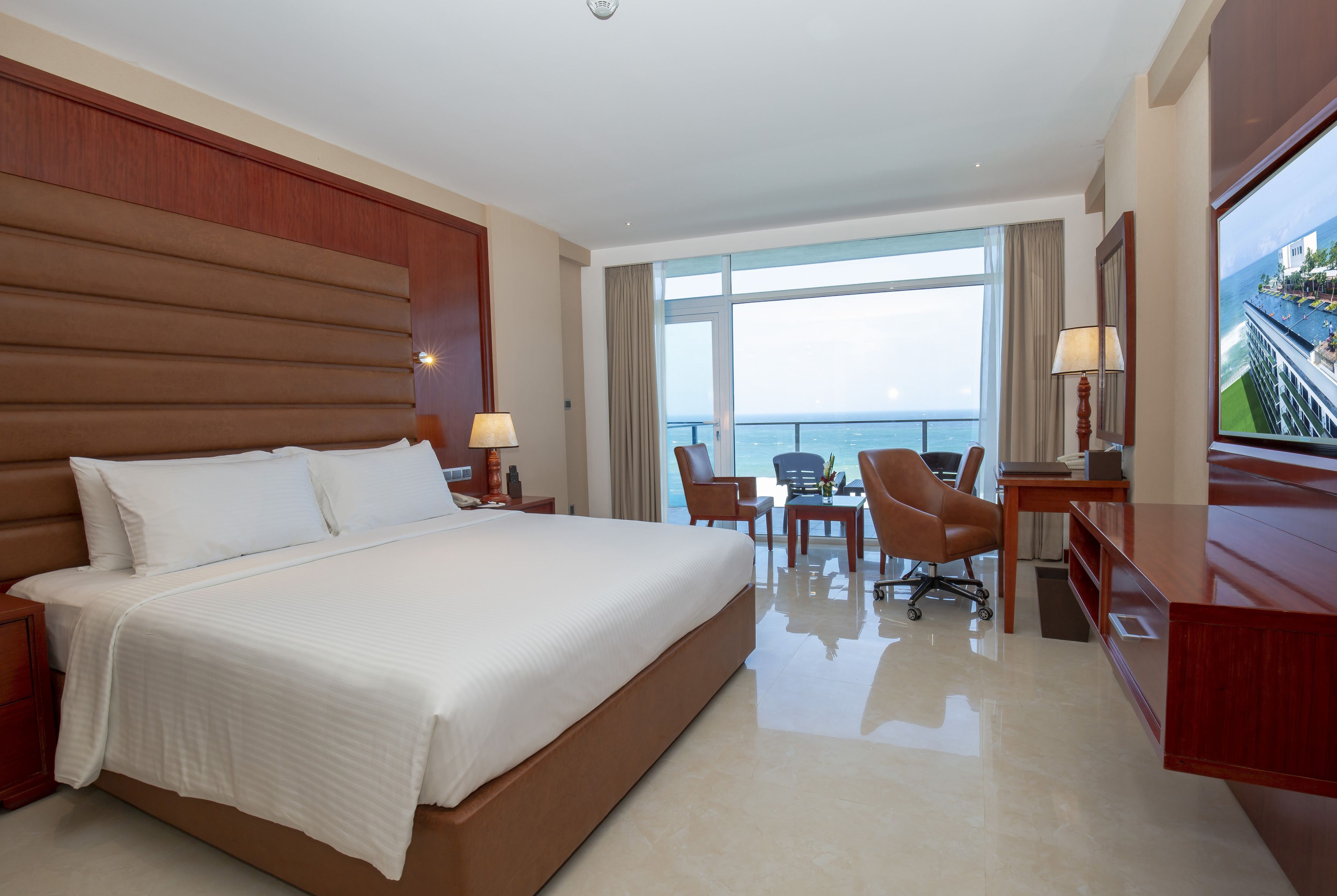 A hotel room with a large bed, a desk, two chairs, and a view of the ocean.