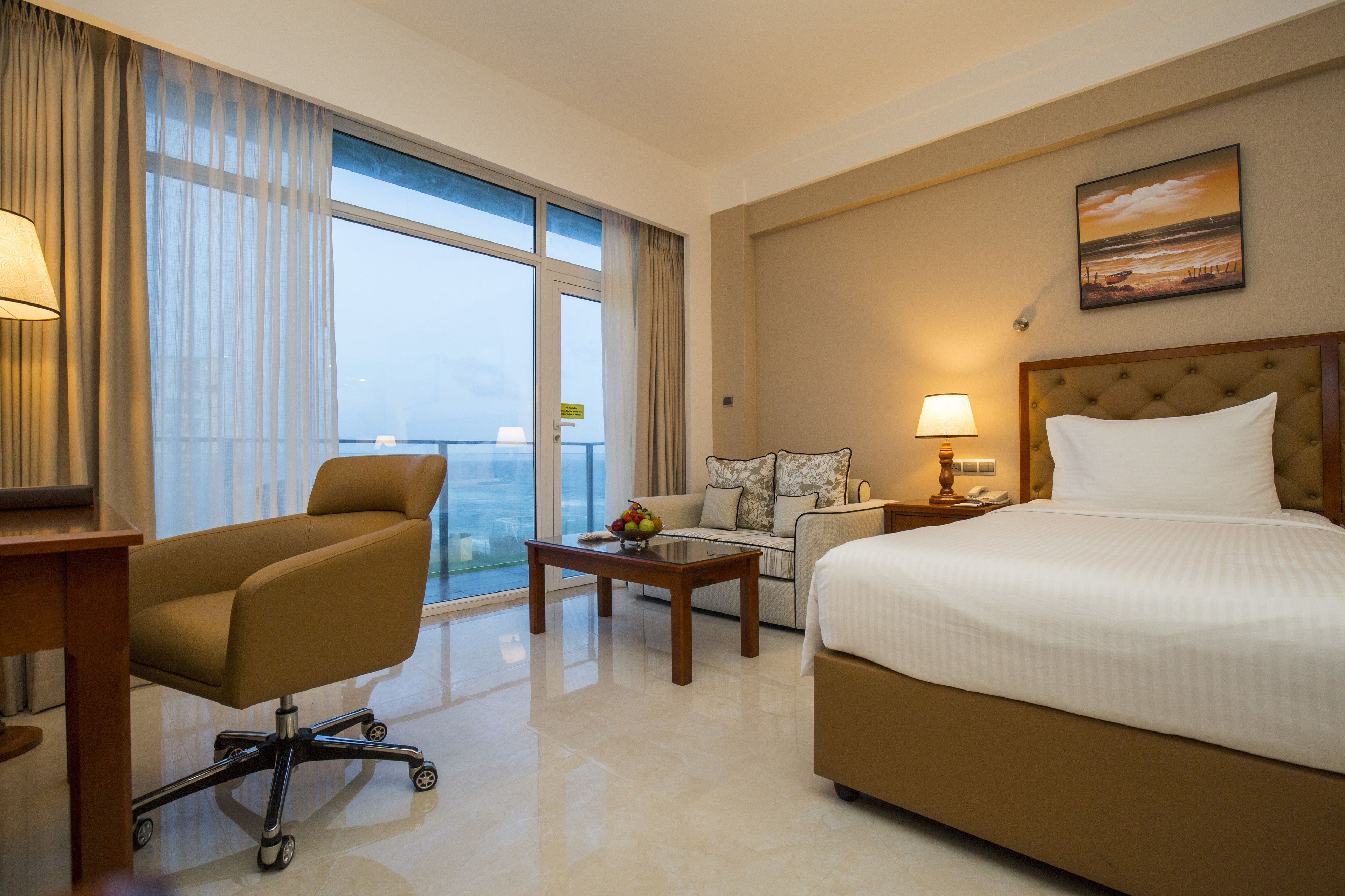 Habitación de hotel con cama, escritorio, sillón, sofá y vistas a la ciudad.