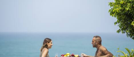 Dos personas en un entorno de piscina, con una cesta de frutas entre ellas.