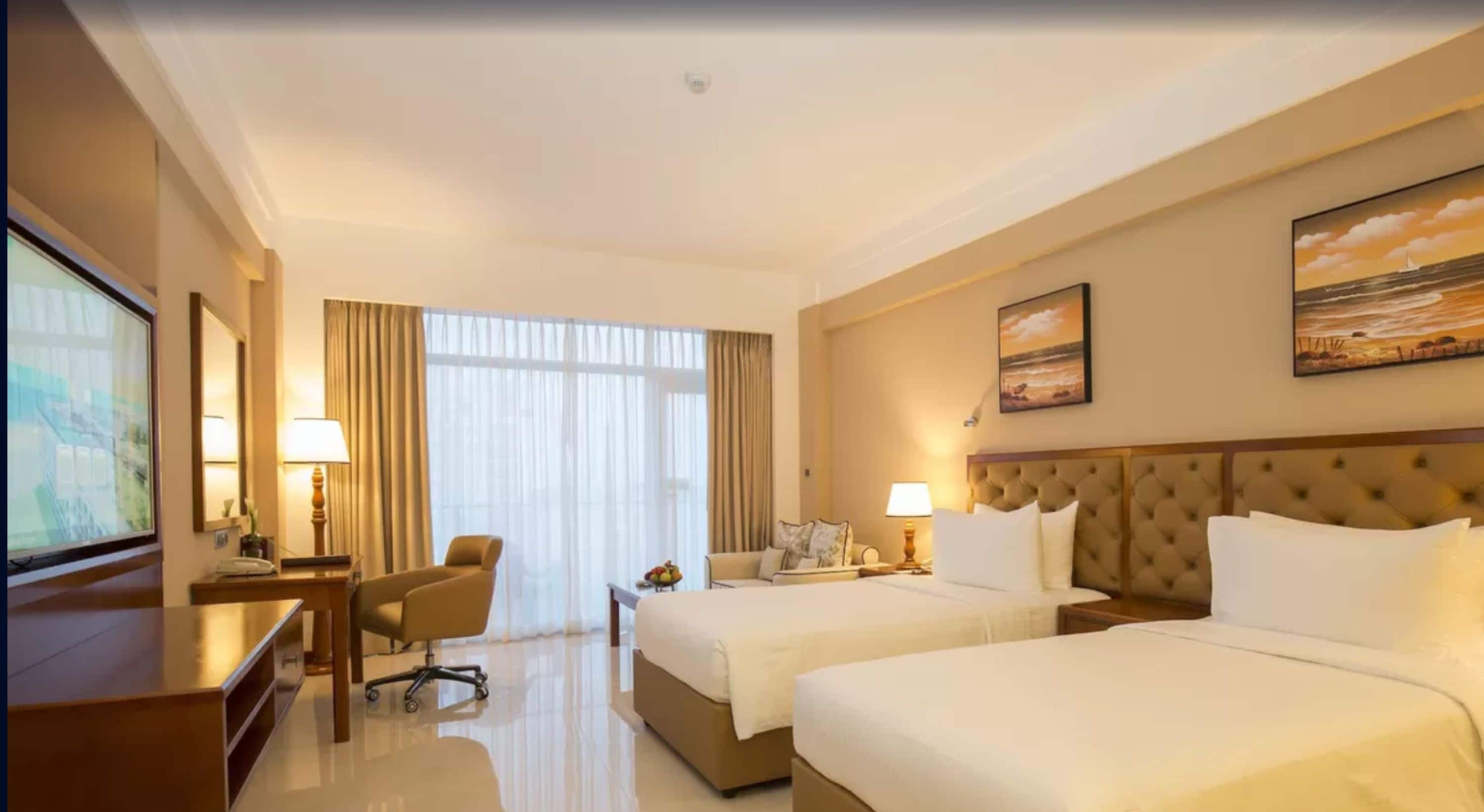 Habitación de hotel con dos camas, un escritorio, una silla y un televisor.