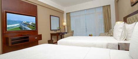 A hotel room with two beds, a TV, a desk, and a large window with curtains.