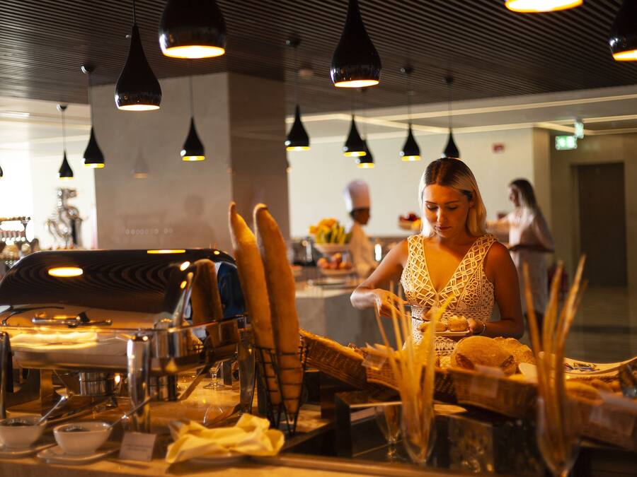 Interior de restaurante con lámparas colgantes, una barra de buffet y un chef al fondo.