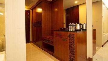 A hotel room with a wooden wardrobe, a small seating area, and a counter with water bottles and a kettle.