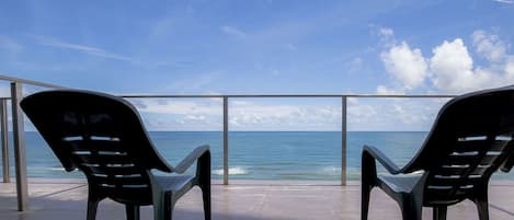 Two black chairs facing a sea view through a glass railing.