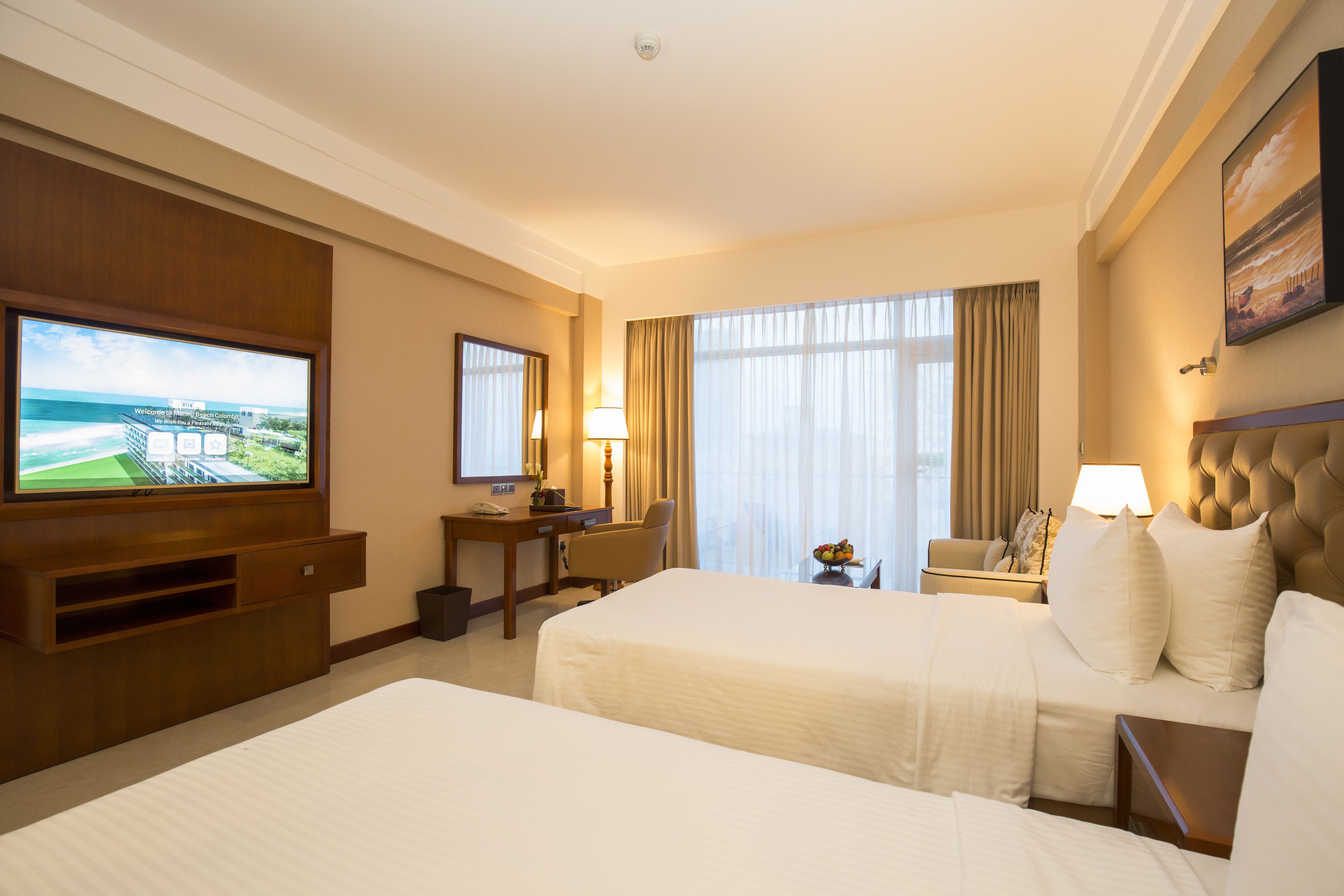 Una habitación de hotel con dos camas, un escritorio, un televisor y una ventana con cortinas.