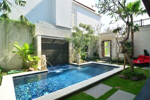 Una piscina con fuente, rodeada de vegetación y un edificio moderno.