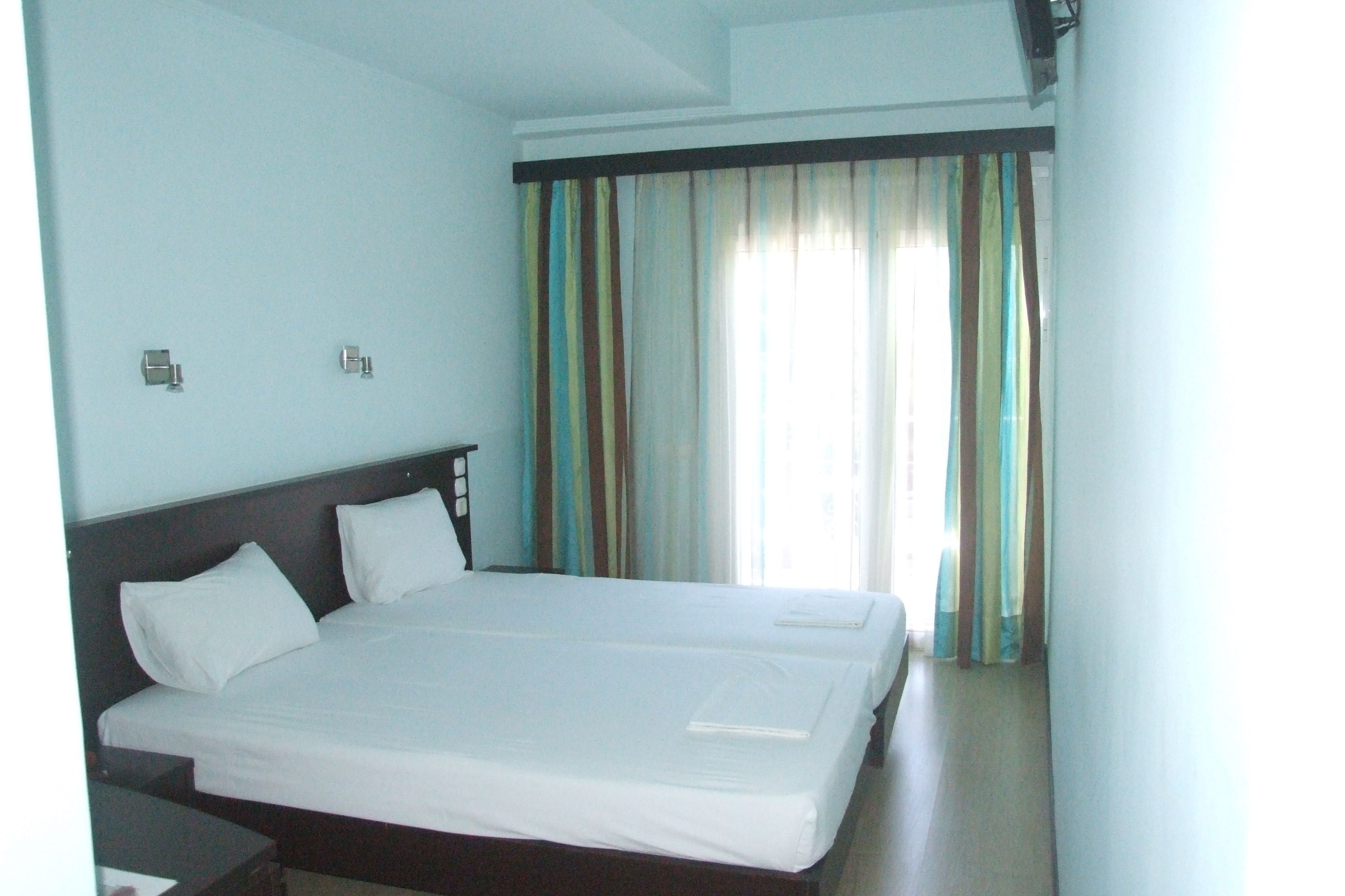 A hotel room with a large bed, two bedside tables, and a window with striped curtains.