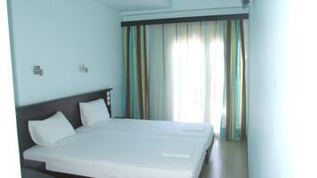 A hotel room with a large bed, two bedside tables, and a window with striped curtains.