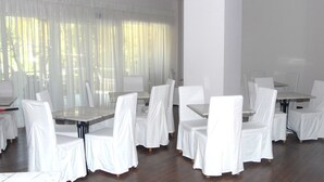 A room with white-covered tables and chairs, large windows with sheer curtains, and a wooden floor. - Hotel George (Patras)