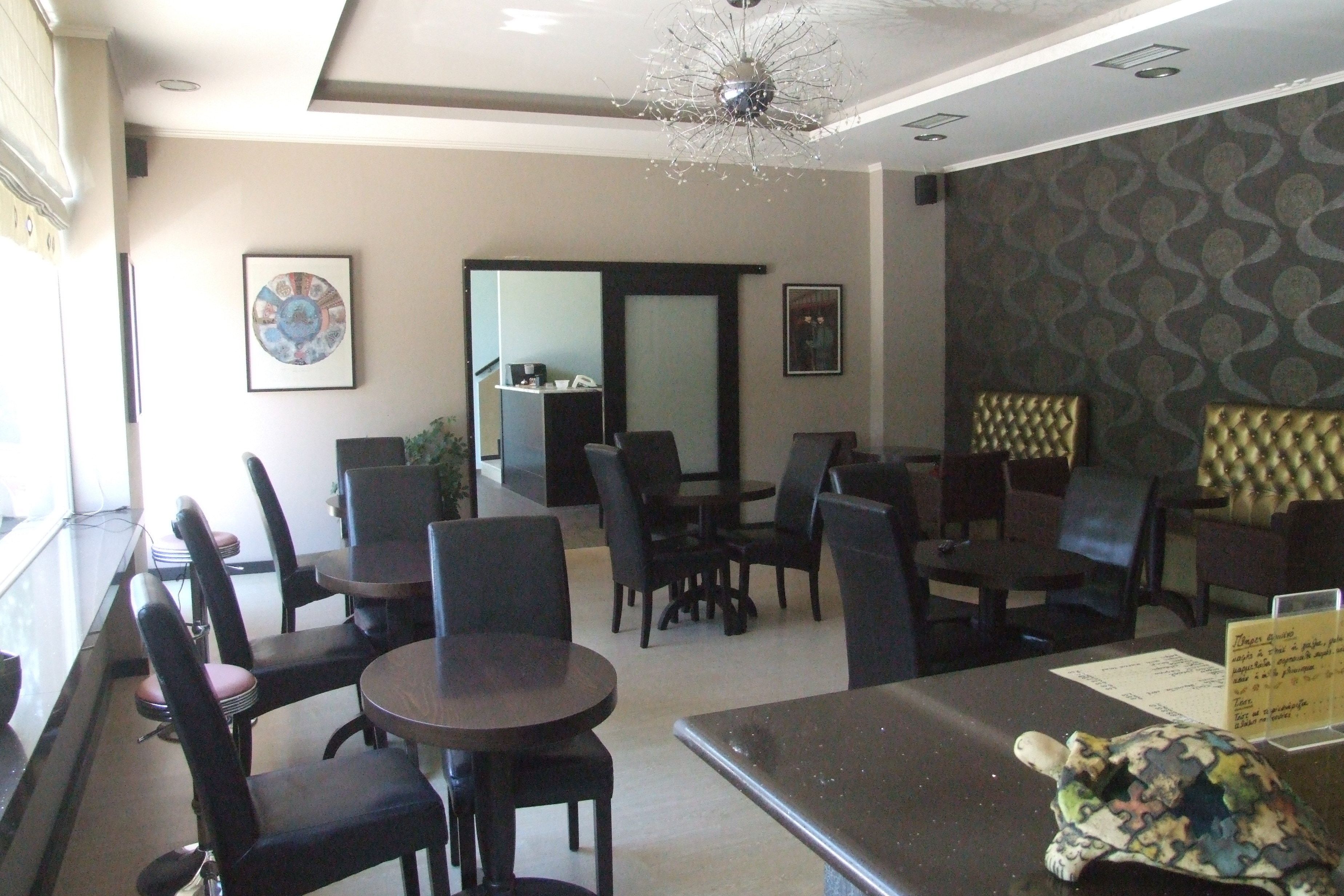 A restaurant with round tables and black chairs, a chandelier, framed artwork on the walls, and a menu stand.