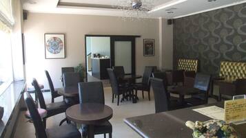 A restaurant with round tables and black chairs, a chandelier, framed artwork on the walls, and a menu stand.