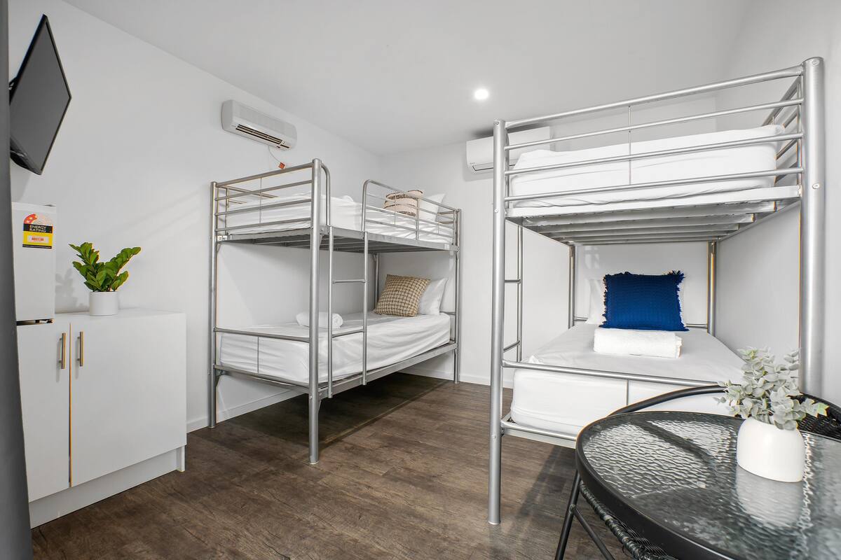 A bunk bed room with a TV, air conditioning, a small plant, and a table with a vase.