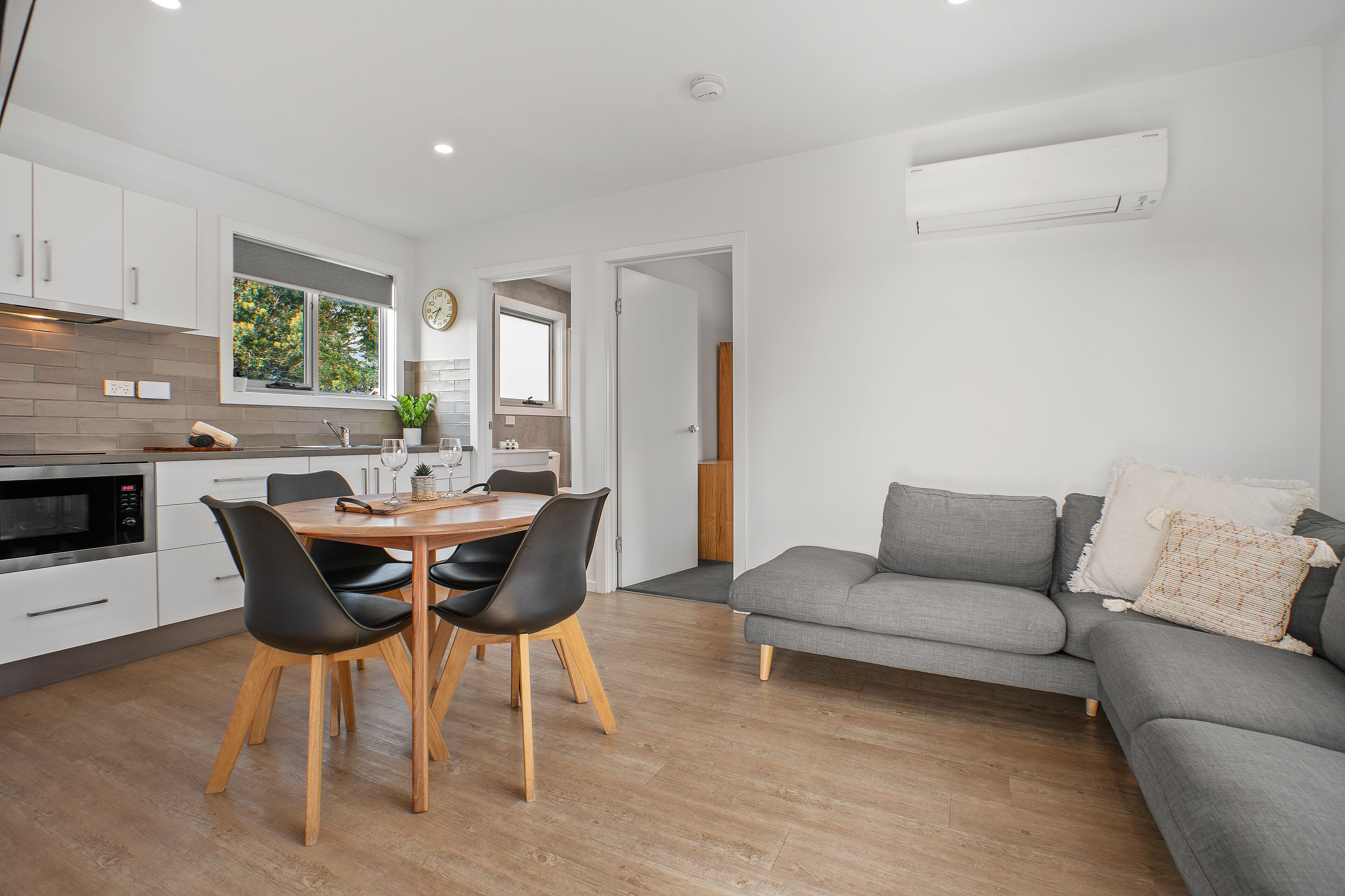 A modern kitchen with white cabinets, a dining table with chairs, and an air conditioning unit mounted on the wall.
