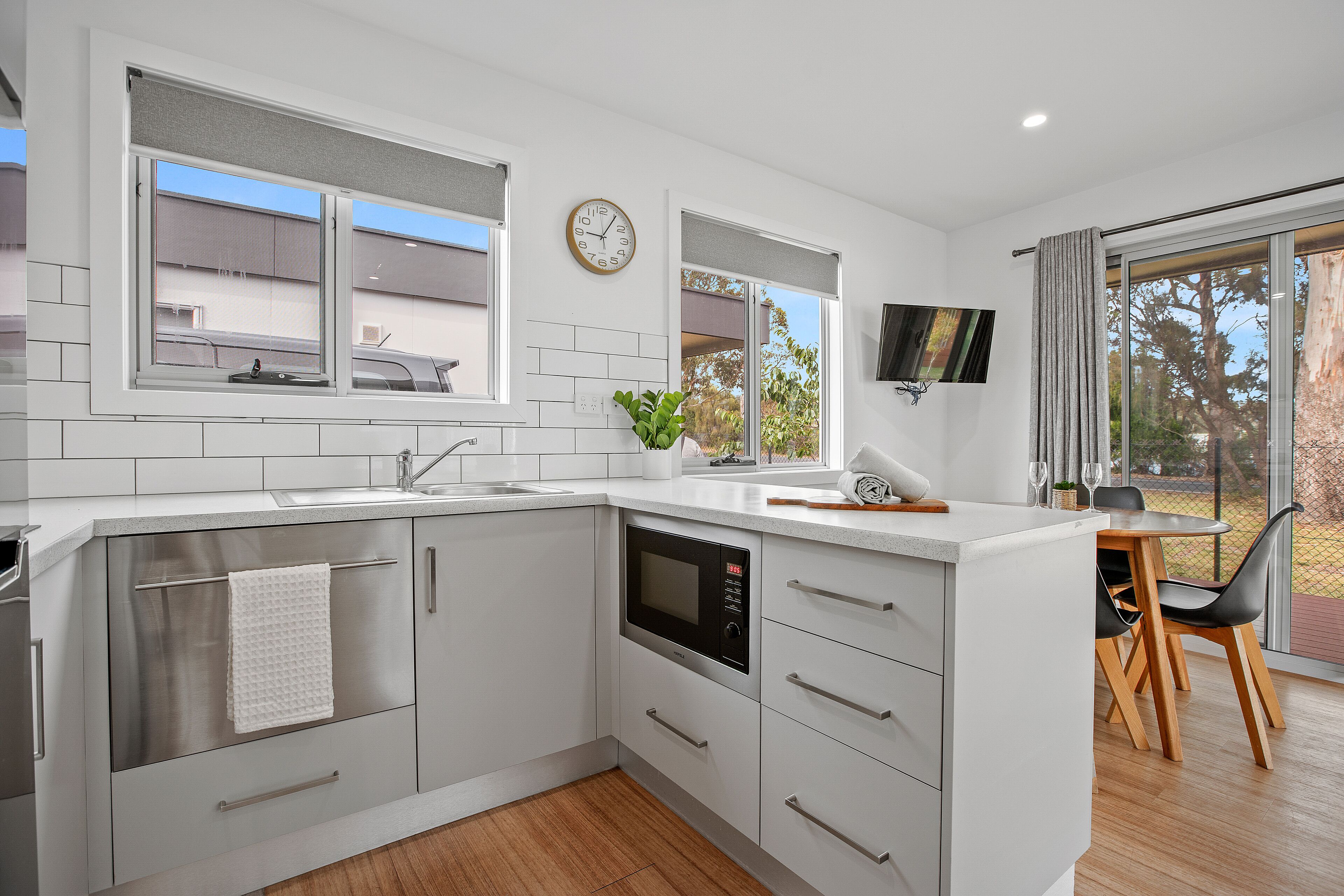 A modern kitchen with white cabinets, a built-in oven, and a dining area with a table and chairs.