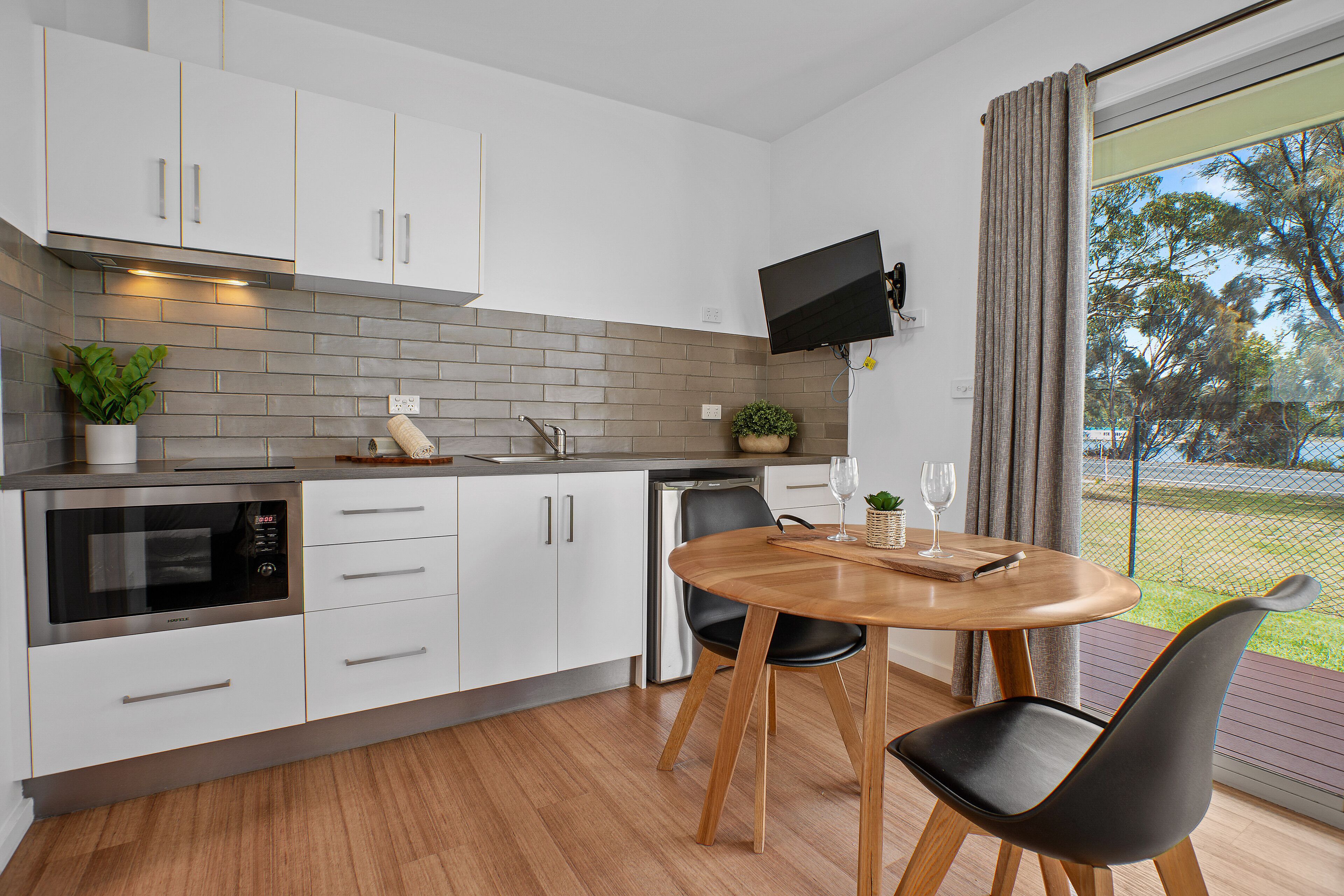 Une cuisine moderne avec des armoires blanches, un four à micro-ondes encastré et un coin repas comprenant une table ronde en bois et deux chaises noires.