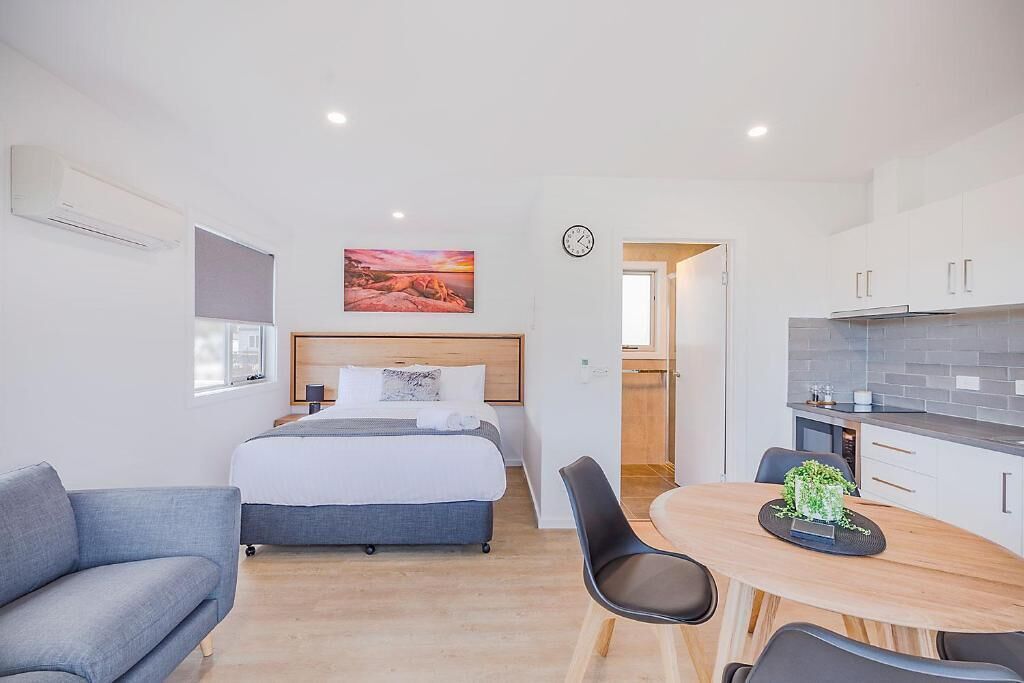 Una habitación de hotel moderna con cama, sofá, mesa de comedor y zona de cocina.