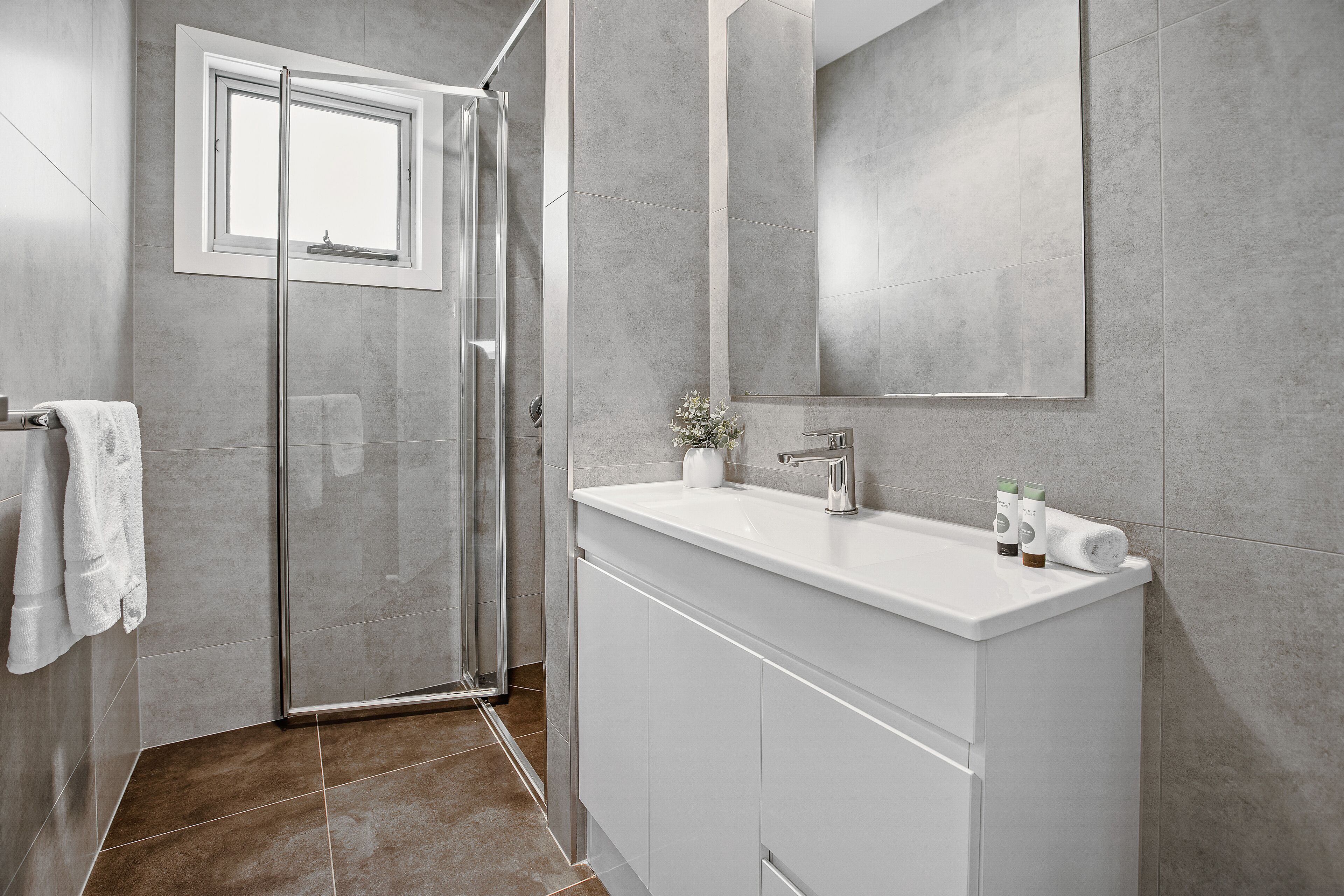 A modern bathroom with a glass shower enclosure, a white vanity with a mirror, and a large mirror above the sink.