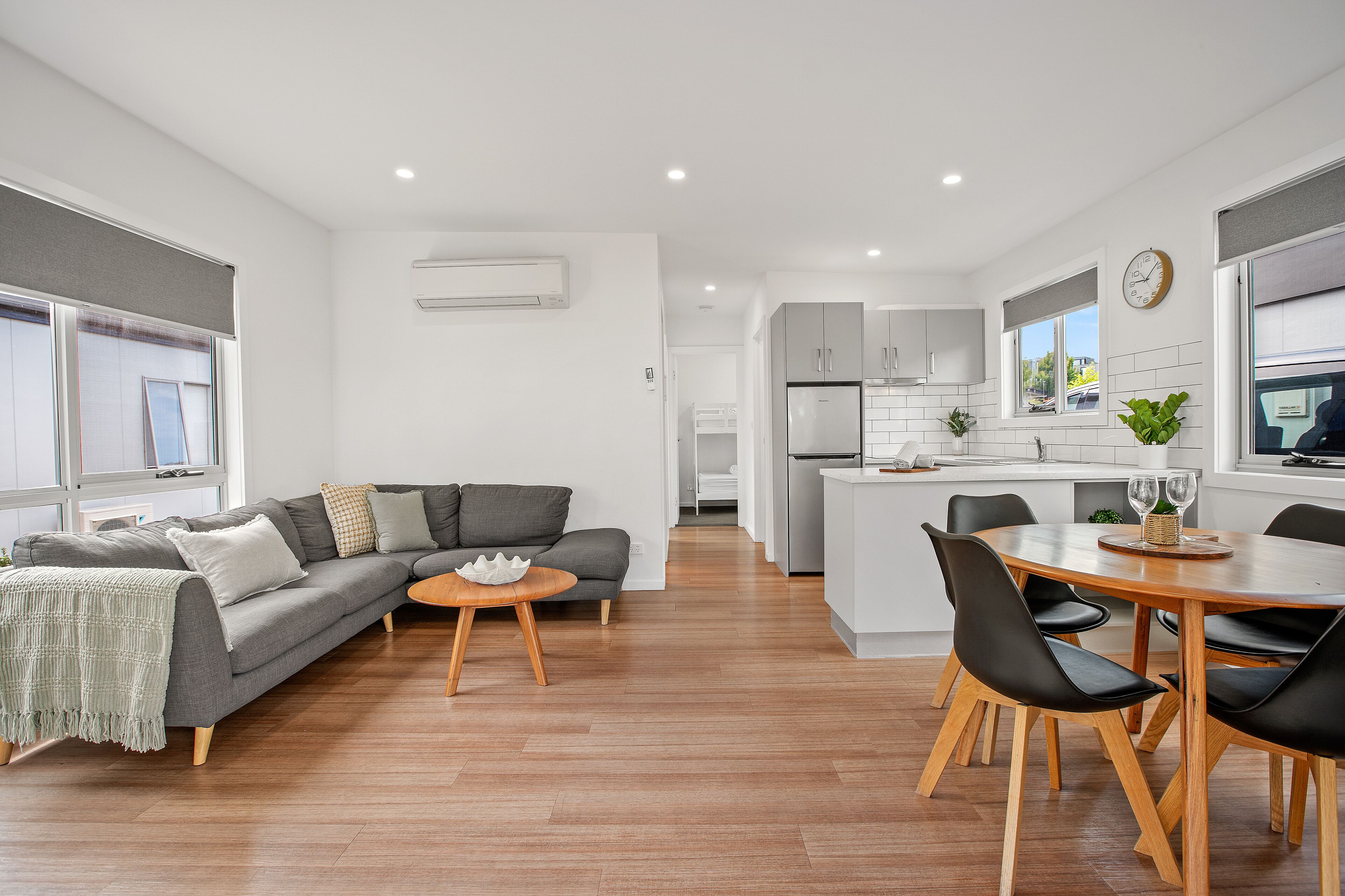 Una sala de estar moderna con un sofá gris, una mesa de centro de madera y un comedor con una mesa de madera y sillas negras.