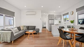 Una sala de estar moderna con un sofá gris, una mesa de centro de madera y un comedor con una mesa de madera y sillas negras.