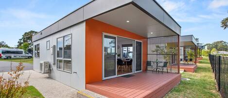 A modern building with a flat roof, large windows, and a covered outdoor area with a table and chairs.