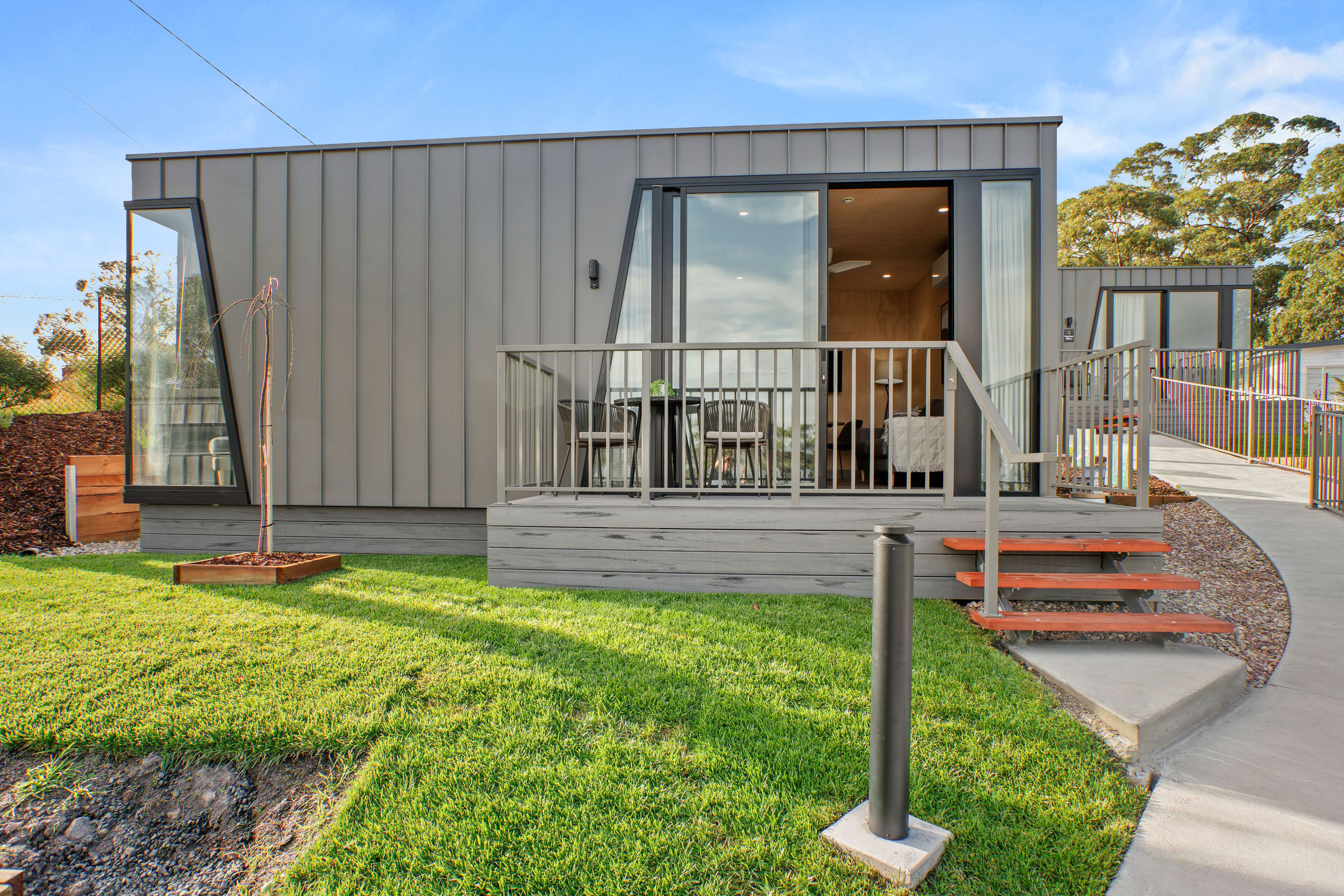 A modern building with a glass door entrance, a covered outdoor seating area, and a small garden.