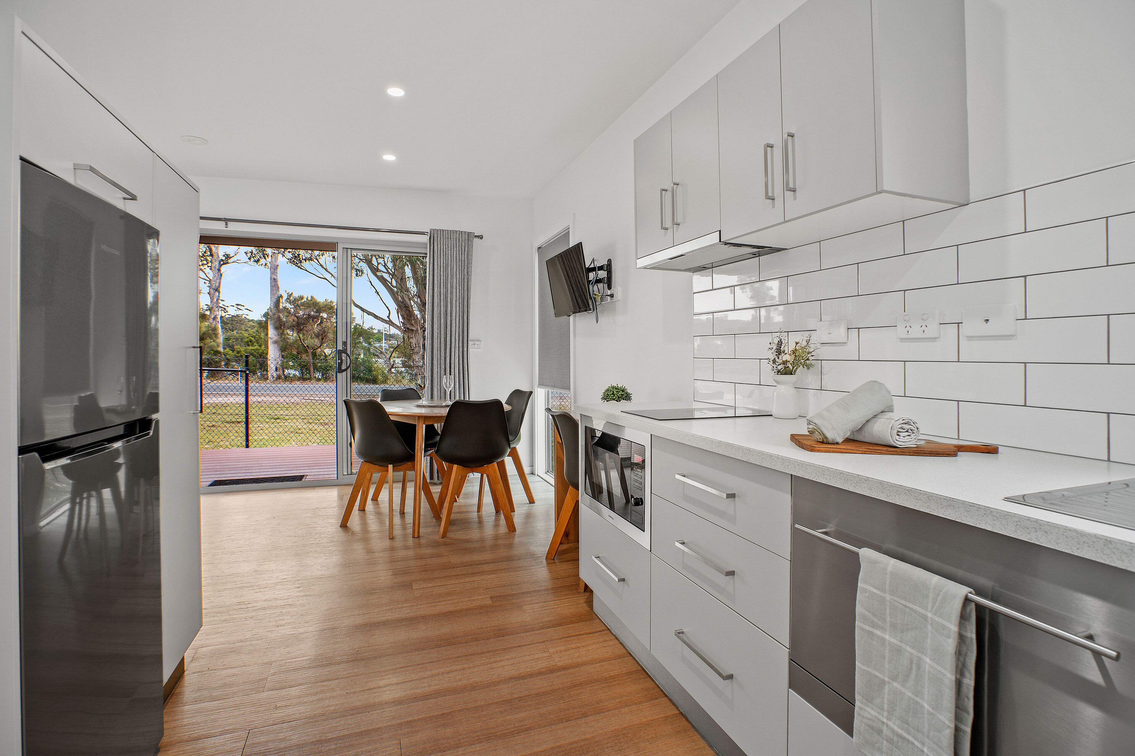 A modern kitchen with white cabinets, a built-in oven, and a dining area with a table and chairs.