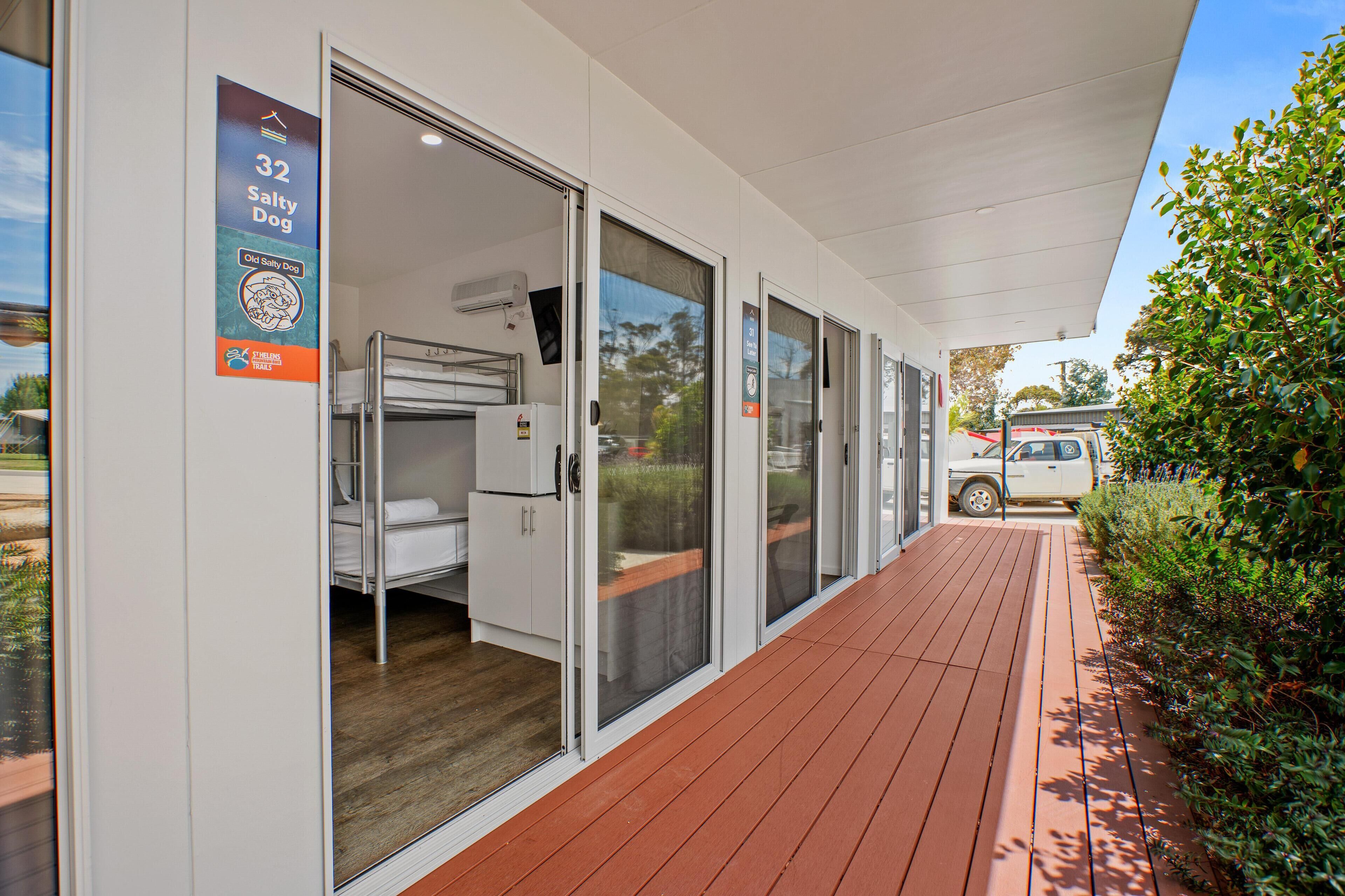 A hotel room with a bunk bed, a small kitchenette, and a sliding glass door leading to a covered outdoor area.