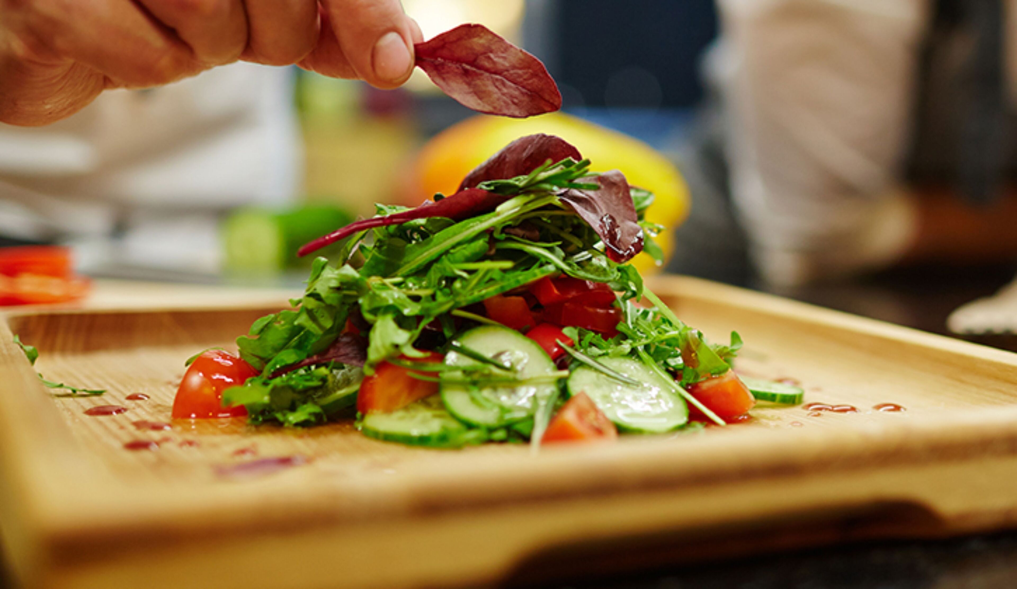 Un chef prepara una ensalada con diversas verduras y hojas sobre una tabla de madera.