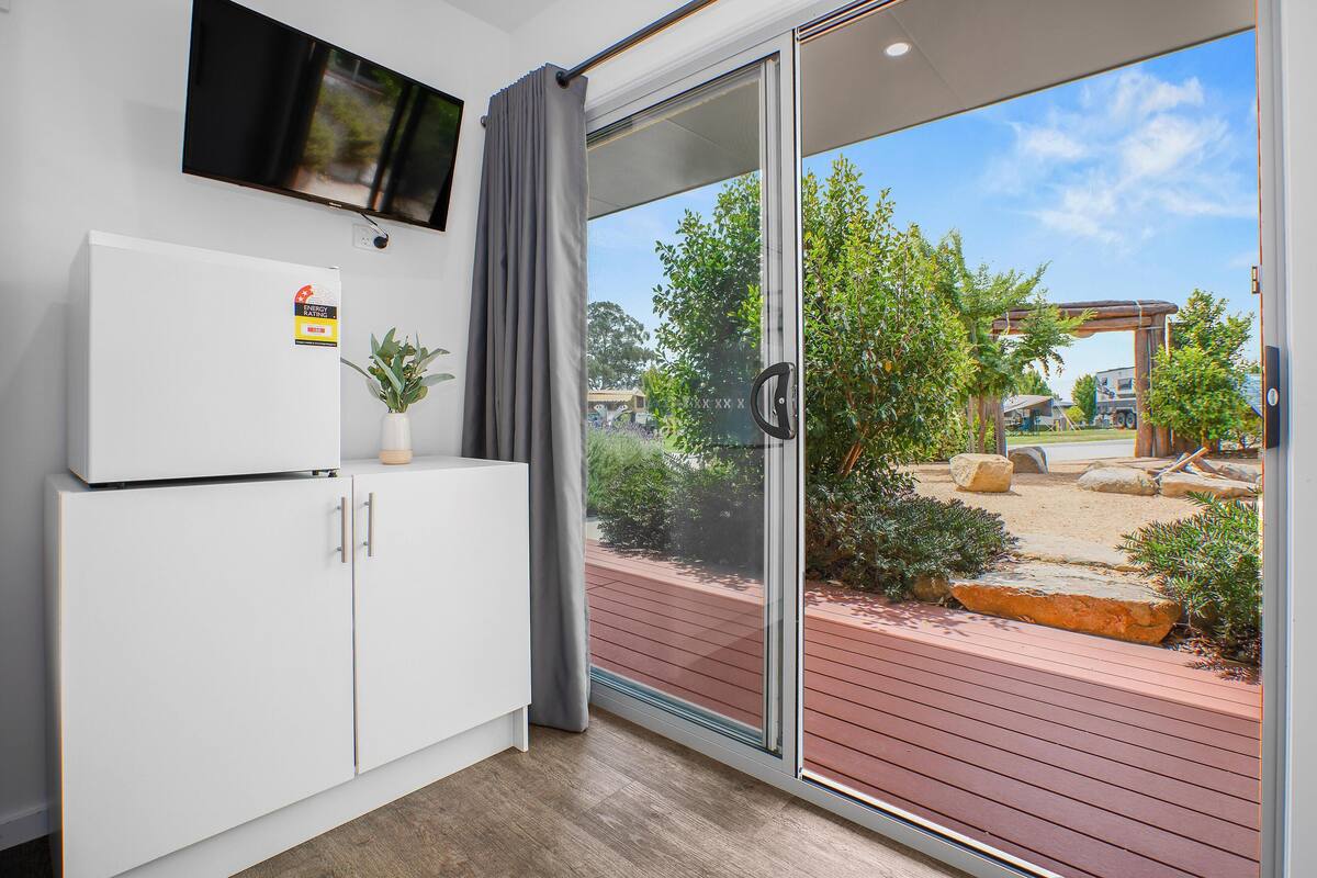 A modern room with a sliding glass door leading to an outdoor area, a white cabinet with a small plant, and a mounted television.