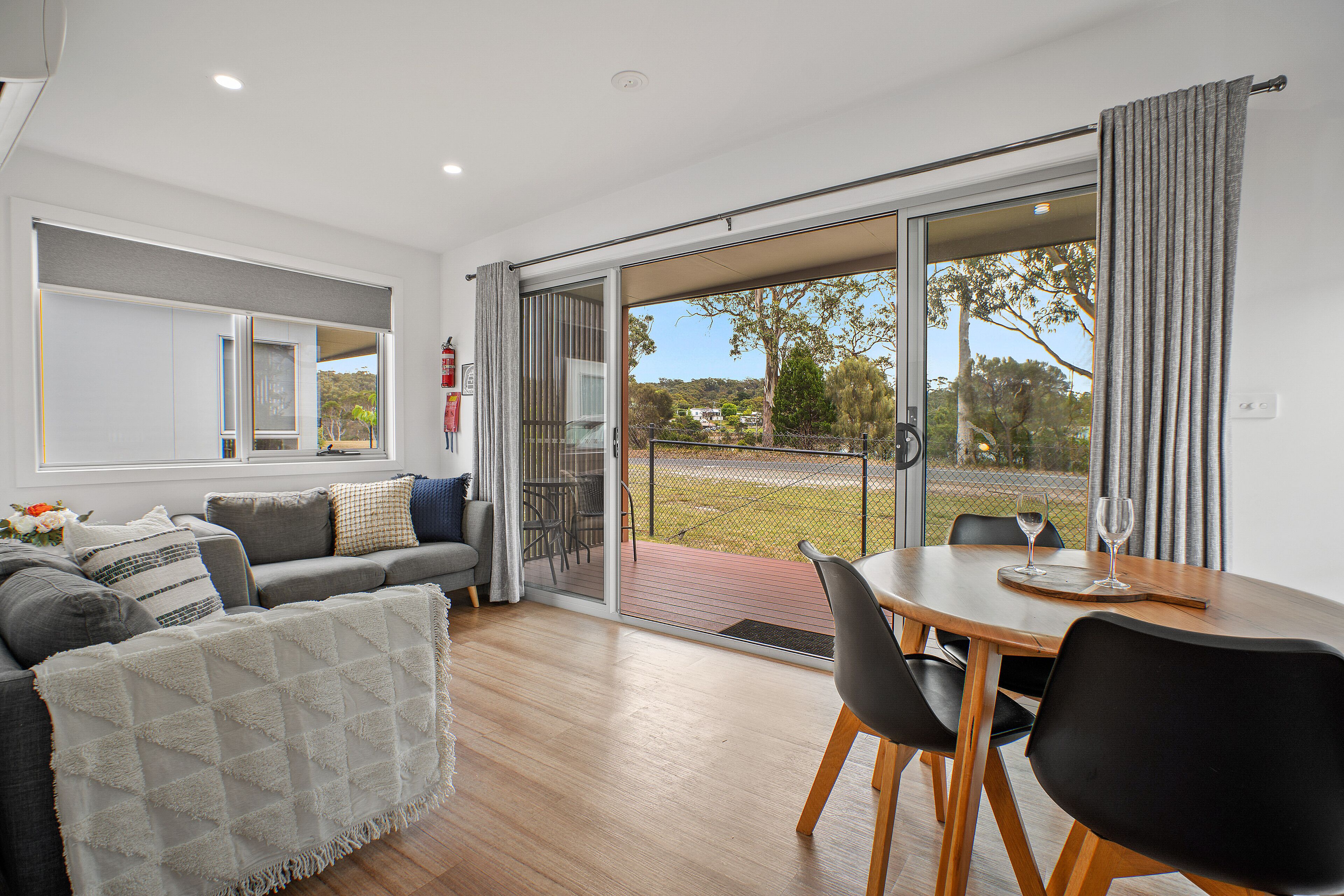 A modern living room with a grey sofa, a dining table with chairs, and a sliding glass door leading to a balcony.