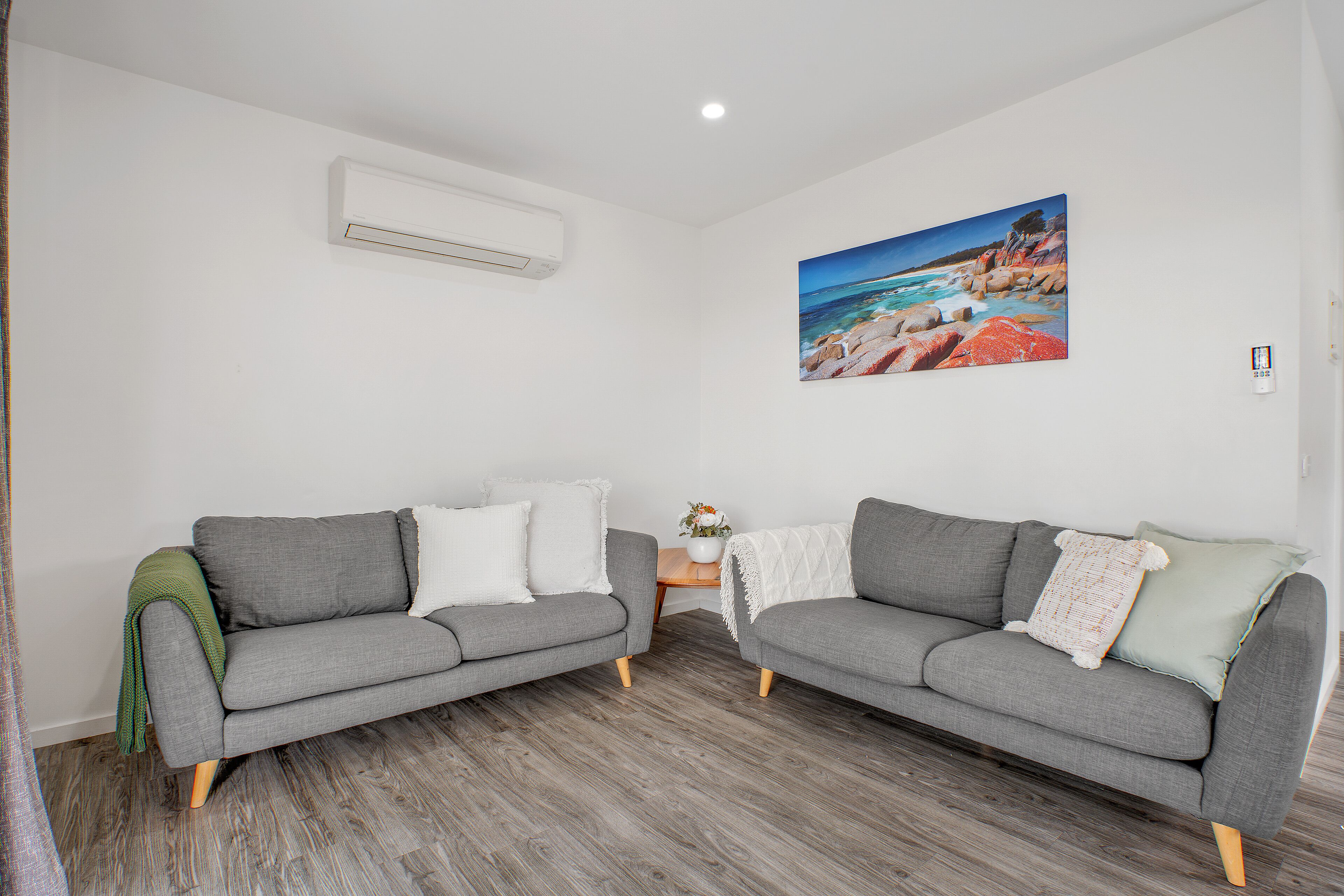A modern living room with two grey sofas, a wooden coffee table, and a painting of a coastal landscape.