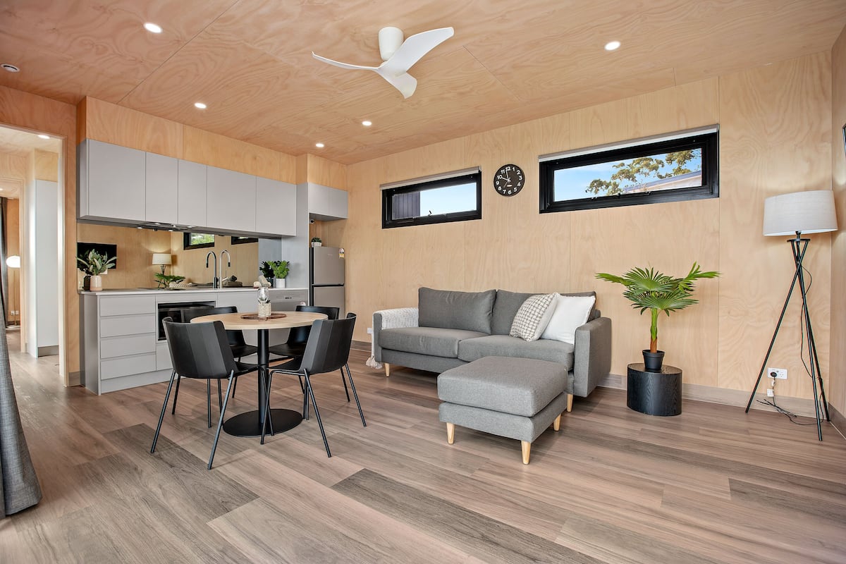 A modern living space with a dining area, grey sofa, and wooden flooring.