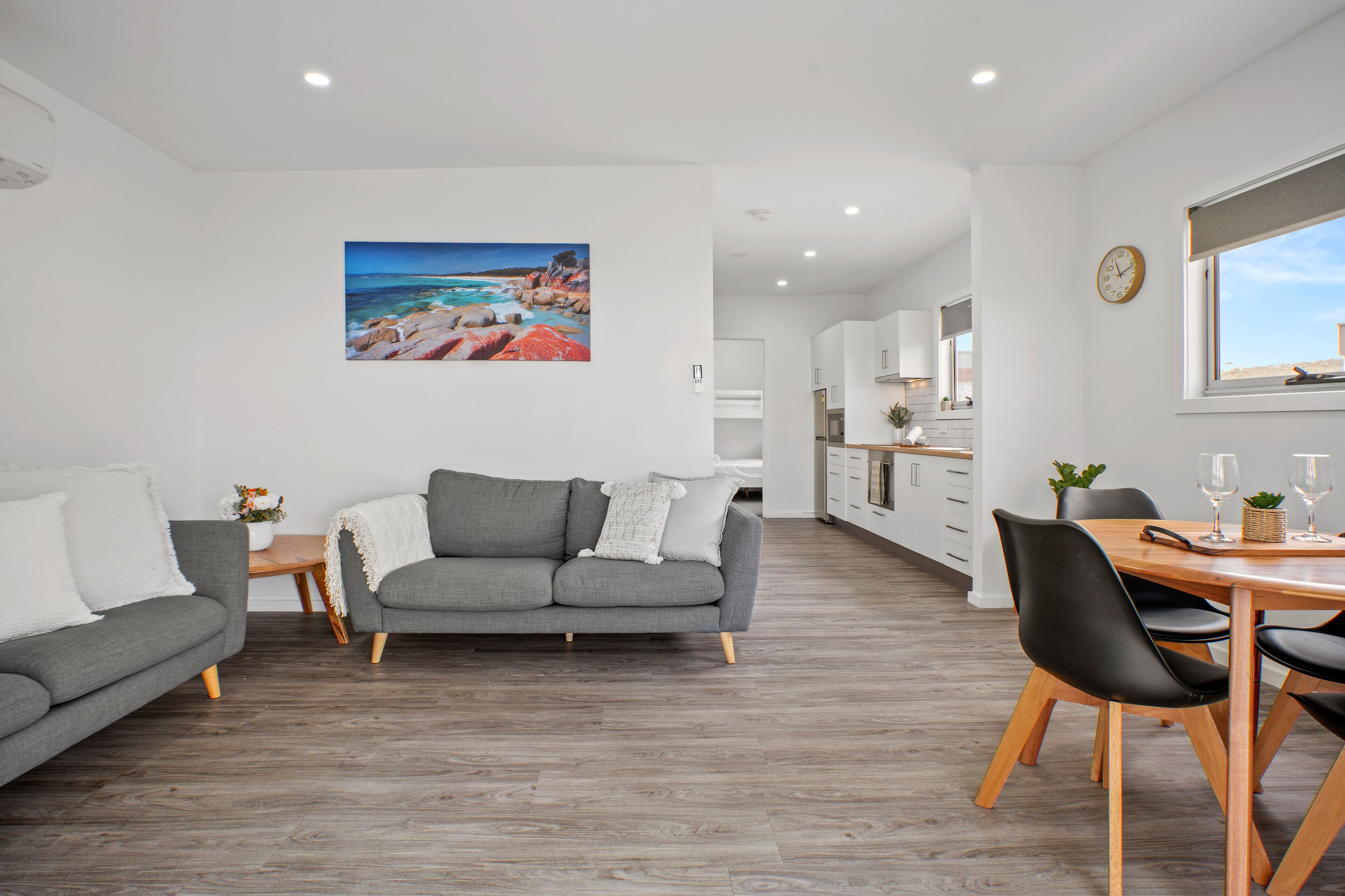 A modern living room with a grey sofa, a dining table with chairs, and a kitchen in the background.