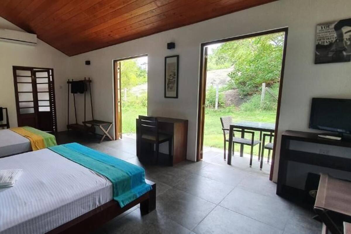 Een hotelkamer met twee bedden, een televisie, een bureau en een balkon met uitzicht op groen.