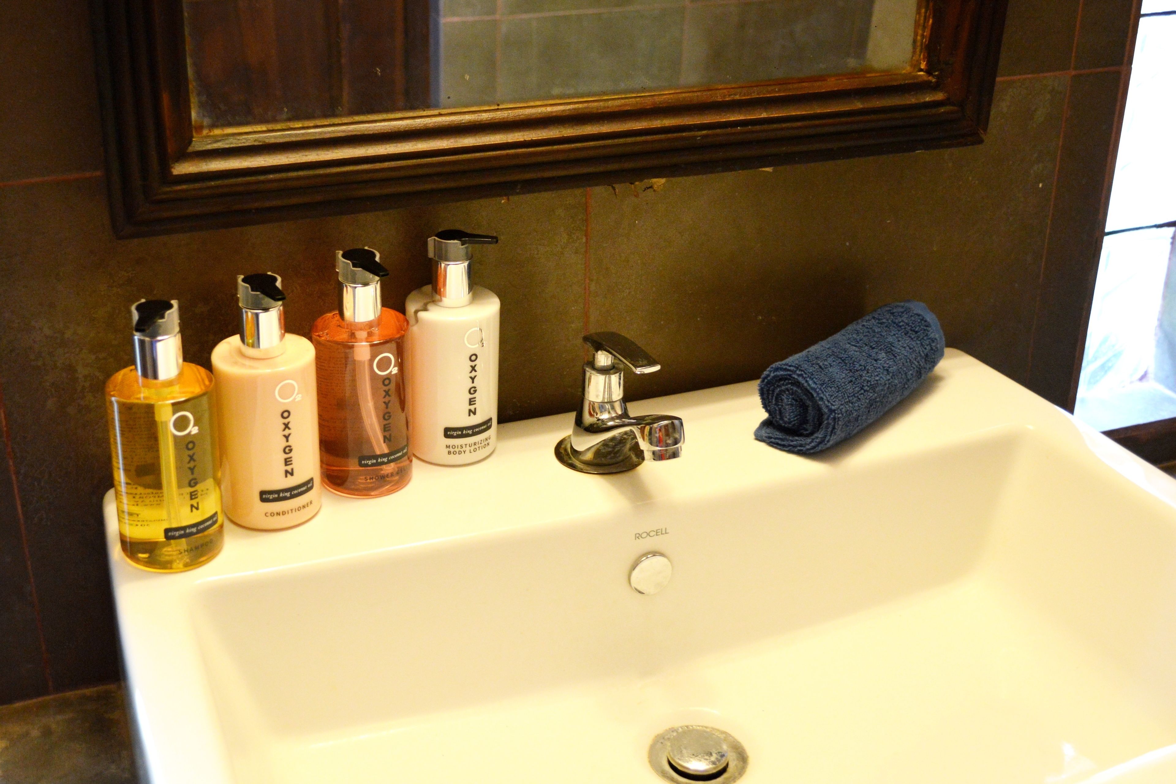 A bathroom sink with four bottles of body care products and a blue towel.