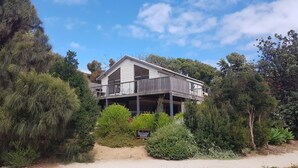 Ein zweistöckiges Strandhaus mit Balkon, umgeben von üppiger Vegetation.