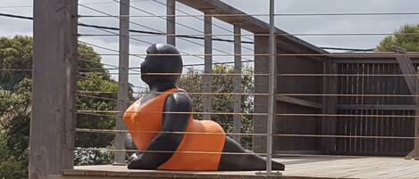 Une sculpture représentant une figure assise, vêtue d’une tenue orange et noire, et entourée d’une clôture métallique.