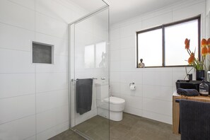 Un baño moderno con cabina de ducha de vidrio, inodoro y tocador con espejo.