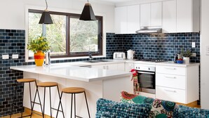 Une cuisine moderne avec des meubles blancs, un grand îlot central doté de tabourets, une fenêtre offrant une belle vue et un pare-feu en carreaux bleus.