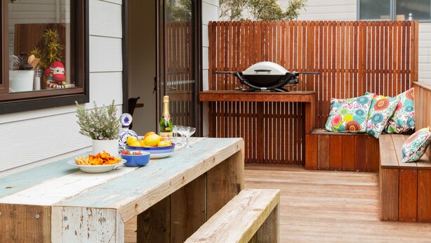 Une terrasse extérieure avec une table en bois dressée pour les repas, un barbecue et un coin salon confortable avec des coussins.