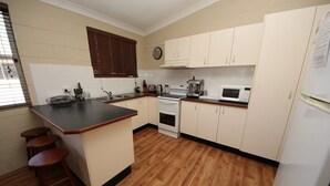 Una cocina con una isla central, suelo de madera, armarios blancos, una estufa, un microondas y un refrigerador.