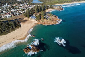 An aerial view of a coastal area with a beach, ocean, and residential buildings. - All Linen Included * Air Conditioning * Central Beach Location * (South West Rocks)