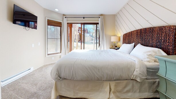 A hotel room with a large bed, a TV mounted on the wall, and a view of a mountainous landscape through the windows.