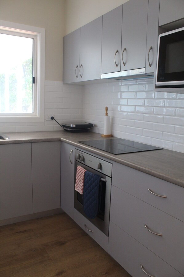 Una cucina moderna con mobili grigi, forno integrato, microonde e una finestra che lascia entrare luce naturale.