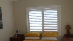 Quarto com cama, mesa de cabeceira, luminária e ventilador de teto.