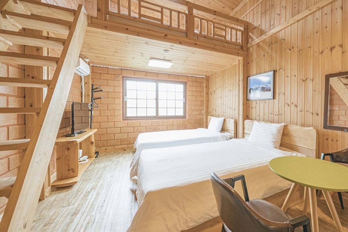 Een houten kamer met een bed, een klein tafeltje en een stoel.